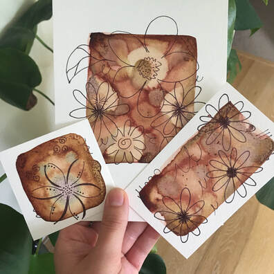 A hand holds three small paintings on paper of flowers.